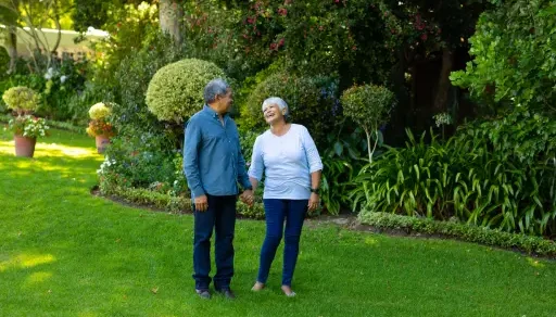 Pareja de personas de la 3a edad disfrutando juntos d eun paseo por un jardín